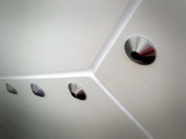 Four metallic, circular radomes with a brushed steel finish and black centers are mounted at a sharp white ceiling or wall corner.